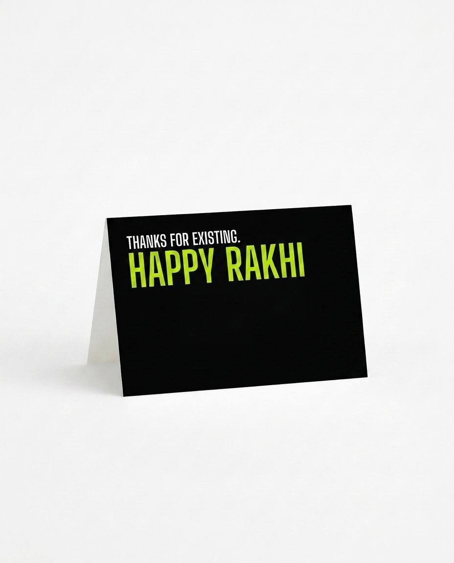 A black rakhi card with a white fold-over back, standing upright on a white surface. The front features the text 'THANKS FOR EXISTING. HAPPY RAKHI.'
